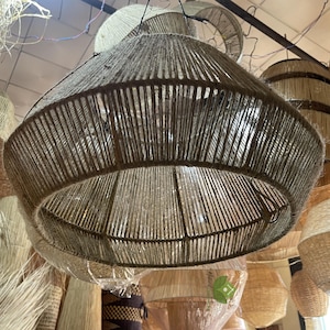 Könnte beinhalten: Ein großer, runder, gewebter Lampenschirm aus Naturfasern hängt von der Decke. Der Lampenschirm ist aus einem hellbraunen Material gefertigt und hat eine leicht strukturierte Oberfläche. Der Lampenschirm ist von anderen ähnlichen Lampenschirmen umgeben, die alle von der Decke hängen.