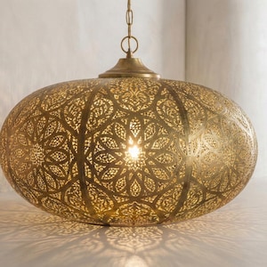 May include: A golden, oval-shaped pendant light with intricate, floral-patterned cutouts. The light fixture hangs from a chain and casts decorative shadows. The lamp is a decorative home decor item.