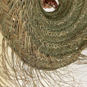 Puede incluir: Primer plano de un sombrero de paja tejido de color marr&oacute;n claro natural. El sombrero est&aacute; hecho de hebras de paja tejidas apretadamente, creando una superficie texturizada. El sombrero tiene un ala ancha y una corona ligeramente puntiaguda.