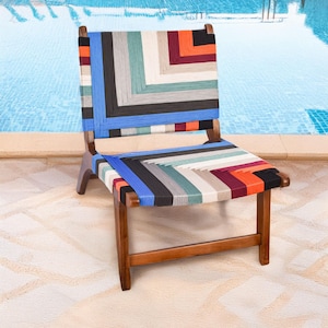 May include: A wooden chair with a woven seat and backrest. The seat and back feature a colorful geometric pattern with blue, black, orange, and white threads. The chair has a natural wood finish and is set against a pool background.