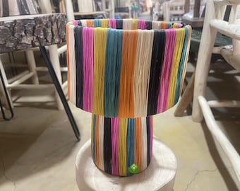 Könnte beinhalten: Eine bunte Lampe mit einem gestreiften Sockel und Schirm. Die Lampe ist aus gewebtem Material gefertigt und hat eine Vielzahl von Farben, darunter Pink, Gelb, Orange, Blau und Schwarz.