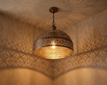 May include: A bronze-colored pendant light fixture with a patterned, dome-shaped shade. The light casts intricate shadows on the surrounding walls. The fixture hangs from a chain and is illuminated by a single bulb.