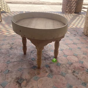 Könnte beinhalten: Ein Holztisch mit runder Tischplatte und drei Beinen. Der Tisch ist aus hellem Holz und hat eine natürliche Oberfläche.