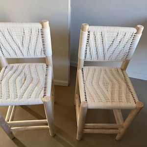 May include: Two light-colored wooden chairs with woven white seats and backs. The chairs have a simple, modern design with rounded legs and back supports. The woven pattern adds texture and visual interest to the chairs.