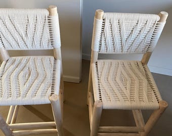 Pode incluir: Duas cadeiras de madeira clara com assentos e encostos brancos tecidos. As cadeiras têm um design simples e moderno com pernas e encostos arredondados. O padrão tecido adiciona textura e interesse visual.
