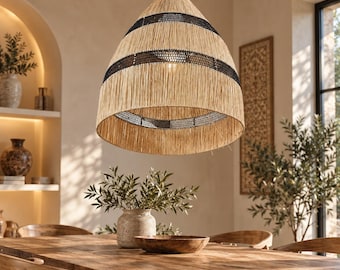 Puede incluir: Una lámpara colgante en forma de campana hecha de fibras tejidas de color beige natural, con dos bandas horizontales distintivas de tejido negro oscuro. La lámpara cuelga de un solo cable negro fino, mostrando una apariencia texturizada.
