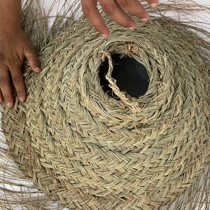 Puede incluir: Un sombrero grande, redondo y tejido con fibras naturales. El sombrero est&aacute; siendo sostenido por las manos de una persona, y el sombrero est&aacute; siendo moldeado en forma de cono.