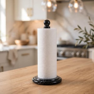 May include: A vertical paper towel holder featuring a circular black marble base and a matching black spherical finial at the top. The holder supports a standard roll of white paper towels, providing a stable structure for kitchen organization.