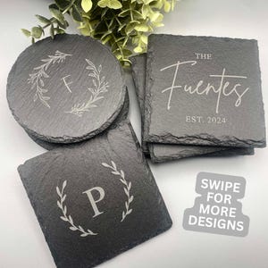 May include: Set of six black slate coasters with engraved designs. One coaster features a wreath with the letter "F" inside. Another coaster features the text "The Fuentes Est. 2024". A third coaster features a wreath with the letter "P" inside.