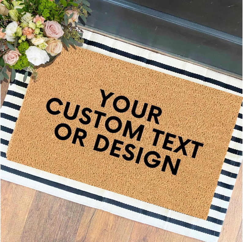 May include: A brown coir doormat with black stripes on the border. The doormat has the text "YOUR CUSTOM TEXT OR DESIGN" printed in black.
