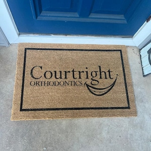 May include: A brown coir doormat with a black border and the text "Courtright Orthodontics" with a smiling mouth graphic.