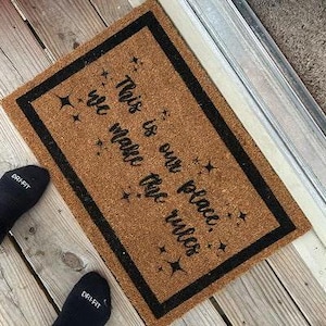 May include: A brown coir doormat with a black border and the text "This is our place. We make the rules." in black lettering. The doormat has a star design.