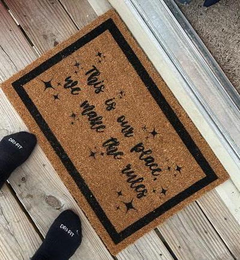 May include: A brown coir doormat with a black border and the text "This is our place. We make the rules." in black lettering. The doormat has a star design.
