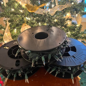 May include: Three spools of black Christmas lights with green wire. The spools are stacked on top of each other. The lights are wrapped around the spools.