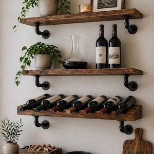 May include: Three dark wood shelves mounted with black industrial pipe brackets. The top shelf holds a potted plant, a candle, and a framed picture. The middle shelf features a potted plant, a glass decanter, and two wine bottles. The bottom shelf holds seven wine bottles.