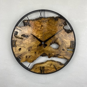 Könnte beinhalten: Eine runde Wanduhr mit einem Zifferblatt aus Naturholz und einem schwarzen Metallrahmen. Das Zifferblatt zeigt ein einzigartiges Holzmaserungsmuster, römische Ziffern und schwarze Zeiger. Die Uhr hat einen Durchmesser von ca. 46 cm.