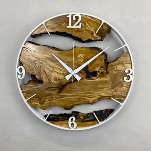 May include: Circular wall clock with a white frame and hands. The clock face showcases natural wood grain patterns in brown and tan hues. White numerals and white clock hands complete the design.