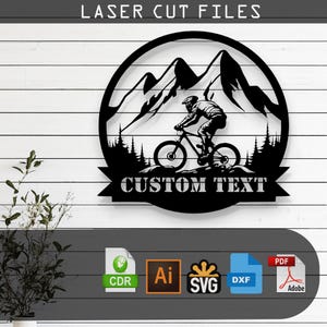 Puede incluir: Silueta en blanco y negro de un ciclista de montaña que recorre un paisaje montañoso. El diseño incluye una pancarta con el texto "CUSTOM TEXT". La imagen es un archivo digital para corte por láser.