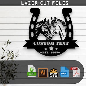 Puede incluir: Herradura de metal negro con dos cabezas de caballo enfrentadas dentro de la herradura. La herradura tiene un banner debajo con el texto "CUSTOM TEXT -EST. 1965-".