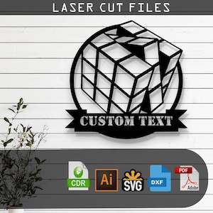 May include: Black laser-cut metal wall art with a Rubik's Cube design inside a circle, with the text "LASER CUT FILES" above and "CUSTOM TEXT" on a banner. Includes file format icons: CDR, AI, SVG, DXF, and PDF.