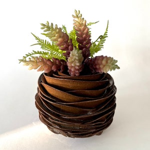 May include: A brown ceramic planter with a ruffled design, holding a small arrangement of green and purple succulents.