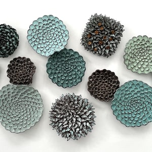 Puede incluir: Una colección de 11 piezas de decoración de pared de cerámica en varios tonos de azul y marrón. Las piezas tienen forma de flores y presentan un diseño texturizado en 3D.