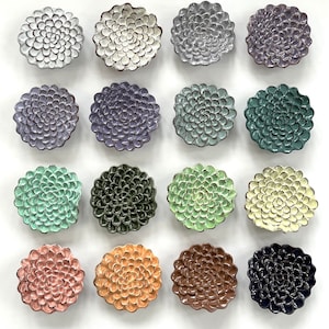 May include: A collection of 15 ceramic dishes featuring a floral design. The dishes come in a variety of colours, including white, grey, green, blue, and pink. Each dish has a unique pattern of overlapping petals.