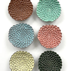 Puede incluir: Seis platos decorativos de cerámica con un diseño floral. Los platos son de varios colores, incluyendo marrón, verde azulado, rosa, amarillo y verde oscuro.