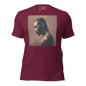 Può includere: Una maglietta girocollo bordeaux con una grafica quadrata di una persona di profilo con una collana. La grafica è nei toni del marrone e del beige, con un design a onde sonore nella parte inferiore. Il marchio "JAMROCK" è stampato in alto.