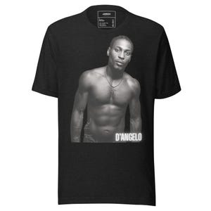 Può includere: T-shirt nero con un'immagine in scala di grigi di un uomo con una collana a croce. L'immagine è di un uomo senza maglietta con il nome "D'ANGELO" stampato sotto. La maglietta ha un'etichetta con la scritta "JAMROCK".