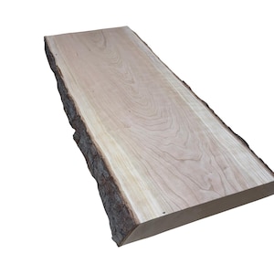 May include: A light-colored, rectangular wooden slab with a live edge. The wood grain is visible, and the bark edge is dark brown. This natural wood slab could be used for a shelf or table top.