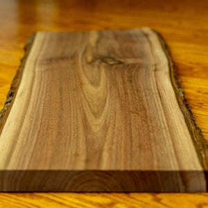 May include: A large, natural wood slab with a live edge. The wood is a rich brown color with a smooth, polished surface. The slab is perfect for use as a cutting board, serving tray, or decorative piece.