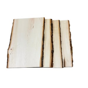 May include: Four rectangular wooden planks with natural bark edges. The planks are light-colored with visible wood grain, and the bark edges are dark brown. The planks are arranged side by side, showcasing their unique textures and shapes.