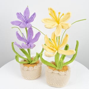 Pode incluir: Dois arranjos de flores de crochê em vasos. Um arranjo tem flores roxas e o outro tem flores amarelas. Os vasos são bege com uma borda marrom.