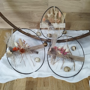 Peut inclure: Trois couronnes de Pâques décoratives avec des fleurs séchées, des plumes et des accents de ficelle. Une couronne est en forme d'œuf, les deux autres sont circulaires. De petits œufs tachetés sont dispersés autour des couronnes.