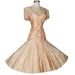 May include: A peach-colored lace dress with a fitted bodice and a full skirt. The dress has a scalloped neckline and short sleeves.