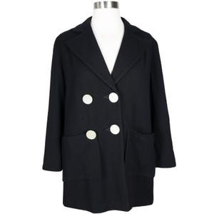 May include: A black double-breasted coat featuring a notched lapel collar, long sleeves, and two large front patch pockets. The coat is fastened with four large, round, white buttons arranged in two vertical rows on the front of the garment.