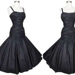 Puede incluir: Un vestido negro sin mangas con un corpiño ajustado y una falda completa. El corpiño tiene un tejido texturizado y fruncido. La falda está hecha de un tejido liso.