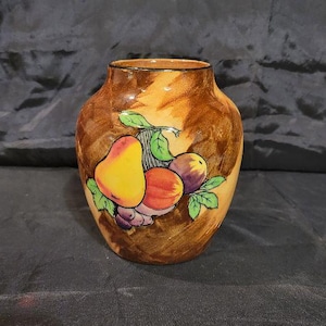 May include: A small ceramic vase with a rounded body and a short neck, featuring a mottled brown and tan glaze. The front is decorated with a hand-painted illustration of a yellow pear, a red peach, and purple grapes with green leaves.
