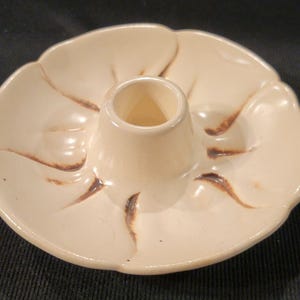 May include: A white ceramic candle holder with a brown glaze design. The holder has a wide base and a central pillar for a candle.