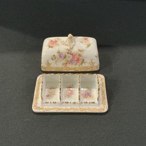 May include: A white porcelain butter dish with a floral design and gold trim. The dish has three compartments and a lid.