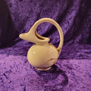 May include: A white ceramic pitcher with a brown swirl design and a unique, curved handle.