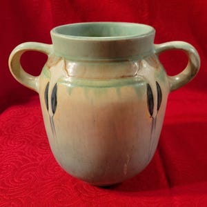 Pu&ograve; includere: Un vaso in ceramica smaltata verde e crema con due manici e un design floreale stilizzato.