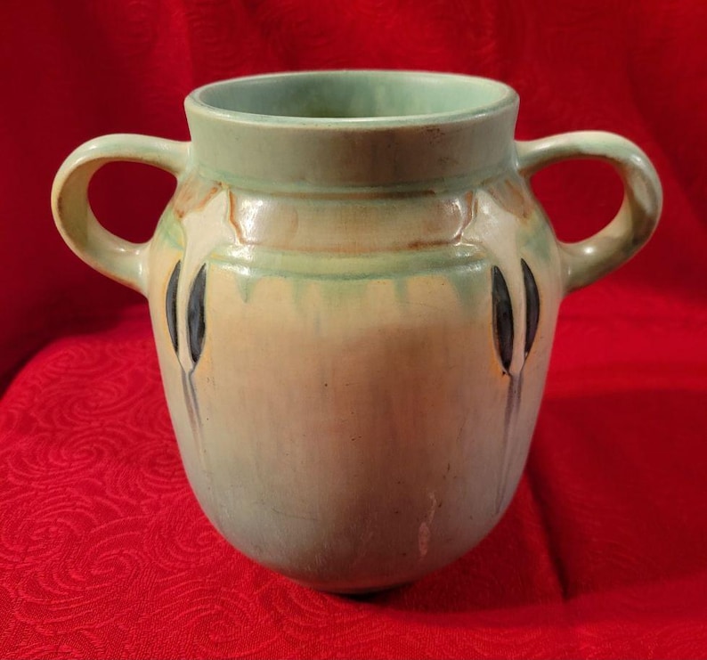 Pu&ograve; includere: Un vaso in ceramica smaltata verde e crema con due manici e un design floreale stilizzato.
