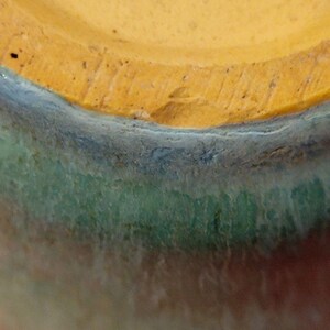 May include: Close-up of the bottom of a ceramic vase with a multi-colored glaze. The glaze is a gradient of orange, green, blue, and yellow.
