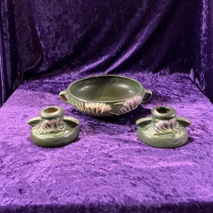 May include: A set of three green glazed ceramic pieces with floral designs. The set includes a bowl with two handles and two candle holders.
