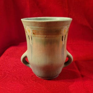 May include: A green ceramic vase with two handles and a decorative design of white flowers and brown lines.