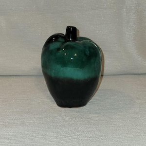 May include: A ceramic apple figurine featuring a glossy glaze with a two-tone color scheme. The upper portion is a vibrant teal green, while the lower section transitions into a deep, solid black. A small, dark black stem sits atop the apple.