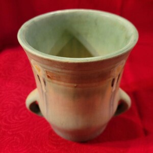 May include: A green ceramic vase with two handles and a decorative design. The vase has a light green glaze with brown and blue accents.