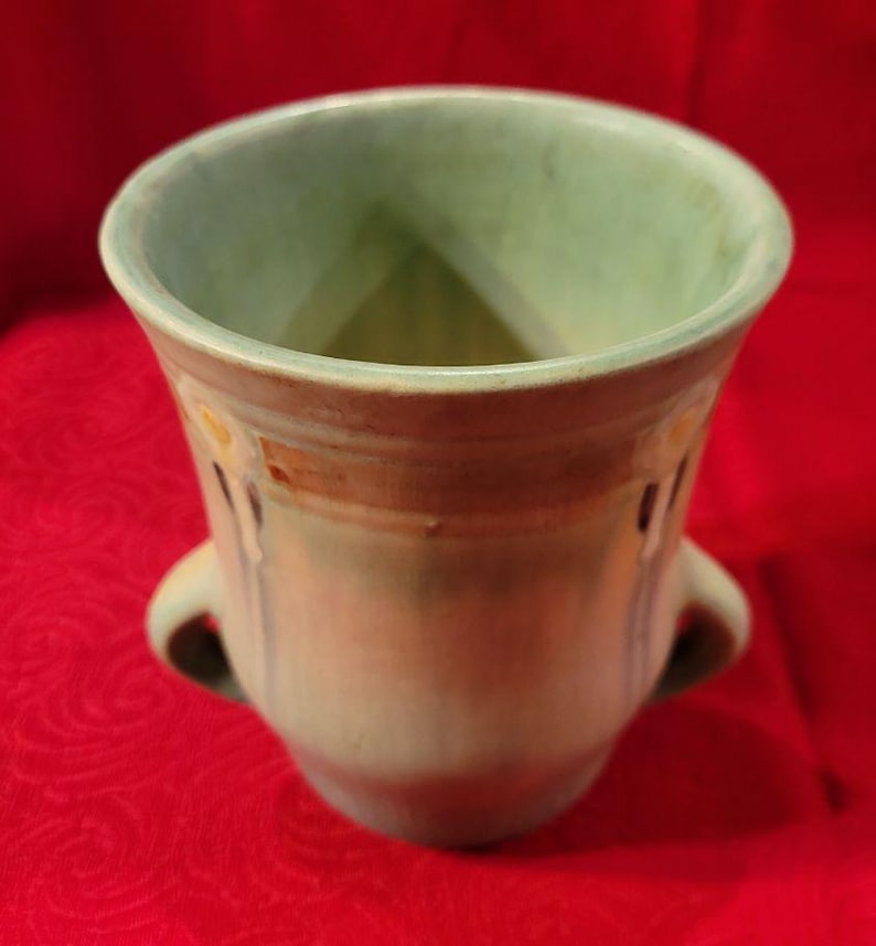 May include: A green ceramic vase with two handles and a decorative design. The vase has a light green glaze with brown and blue accents.